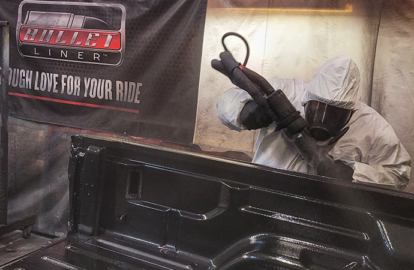 Applicator spraying Bullet Liner protective coating on truck bed.
