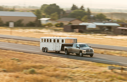 Truck pulling trailer on a road surrounded by farm land.