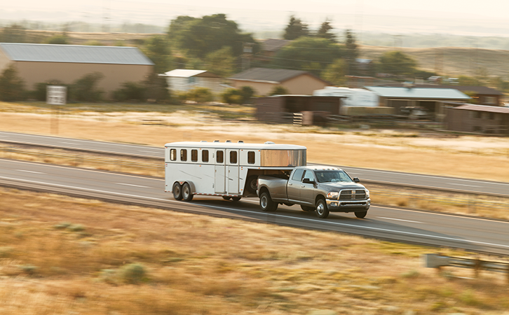 Truck pulling trailer on a road surrounded by farm land.